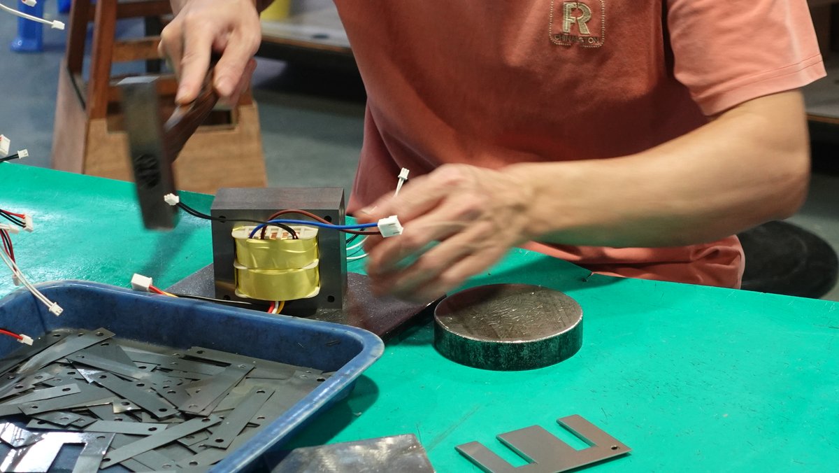 装配工位特写：师傅在工作台为 EI 铁芯变压器插片与整型